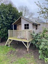 Træ legehus på stolper med terrasse og trappe